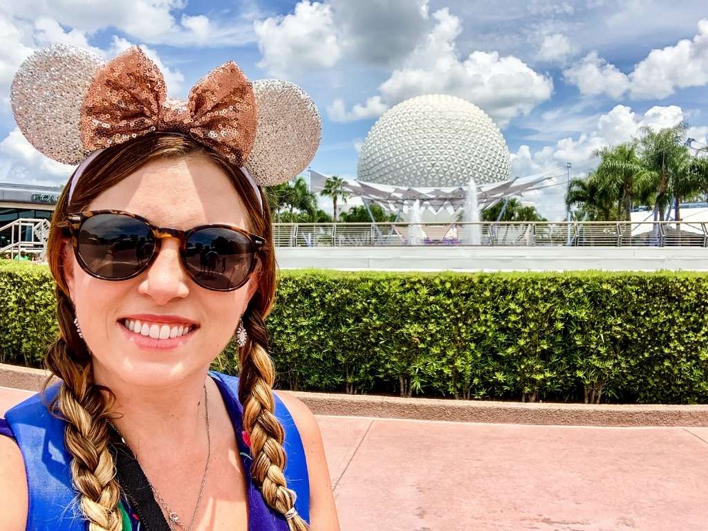 a girl standing in front of the epcot ball